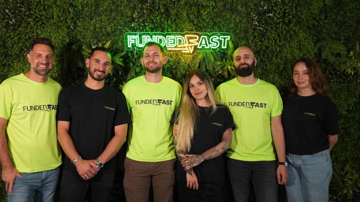 ブランドTシャツを着たFundedFastのバルセロナチームが、緑の植物ウォールとFundedFastのネオンサインの前に並ぶ様子